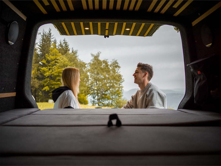 Blick aus dem offenen Heck eines Vans auf zwei Personen im Grünen