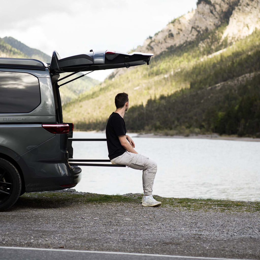 CampBoks Pro 2026 mit ausgezogenen Sitzbänken und sitzender Person. Im Hintergrund ein See mit Bergpanorama.