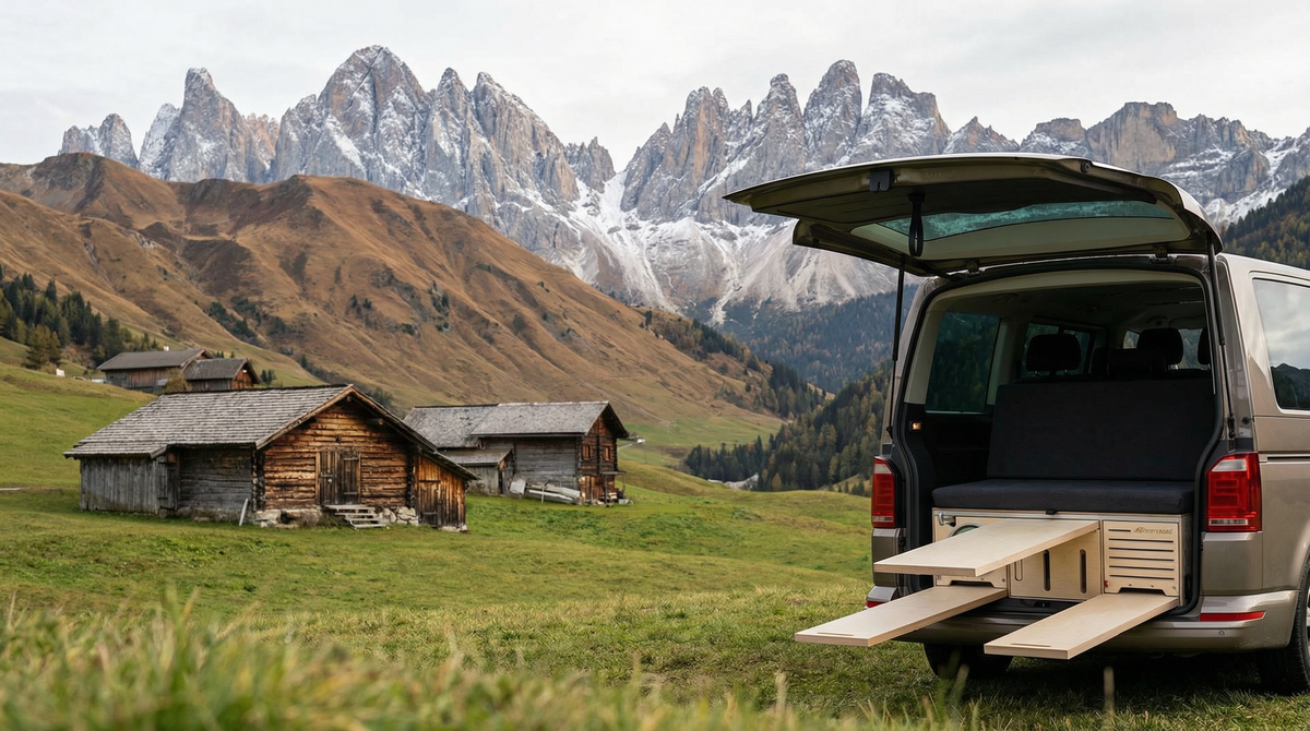 CampBoks im Kofferraum. Im Hintergrund eine Weidelandschaft in den Alpen.